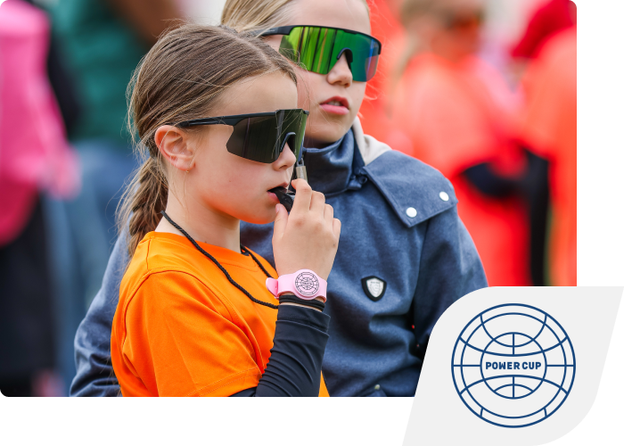 To piger i sportstøj, den ene fløjter i en fløjte. I højre hjørne er PowerCups logo placeret.